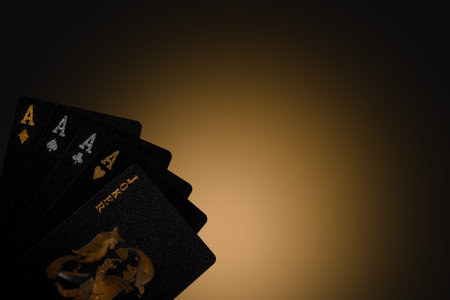 A close up shot of a hand of cards including three aces and a joker on a dark background studio...