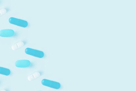 Scattered blue and white capsule pills on a light blue background with ample copy space available.の写真素材