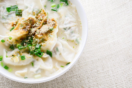 Wonton soup with spring onion served in a white bowl, selective focus