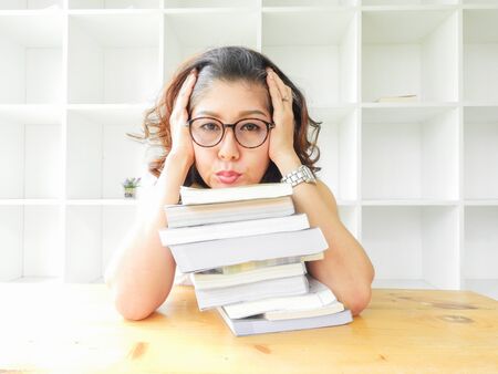 Beautiful women in glasses crushed on the table by a lot of books, very stressed of the study.の写真素材