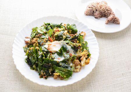 A white plate of delicious Stir-Fried Baegu Leaves or Melinjo with Eggs, served with steamed rice.の写真素材