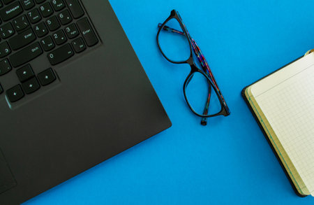 desktop. Laptop, glasses and notepad on a blue background. Mockup diary. Business, freelancing, back to school.の写真素材