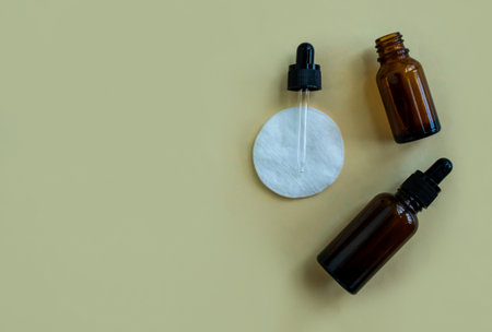 Flat lay bottles with a pipette for cosmetics and a cotton pad on a beige background. Accessories for beauty salon, spa salon. Women's cosmetics, personal care.の写真素材