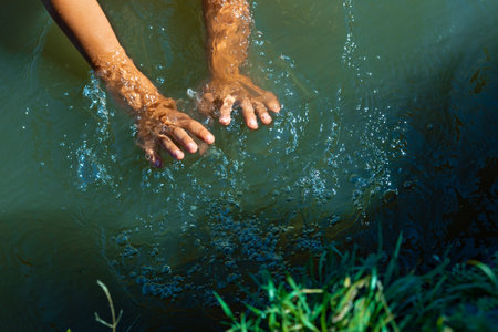 The childs hands spray dense green water in the lake. Summer activity for children - a game with clear waterの写真素材