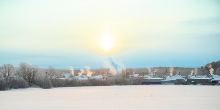 Winter frosty sunny day. Smoke comes out of the pipes above the village houses during heatingの写真素材