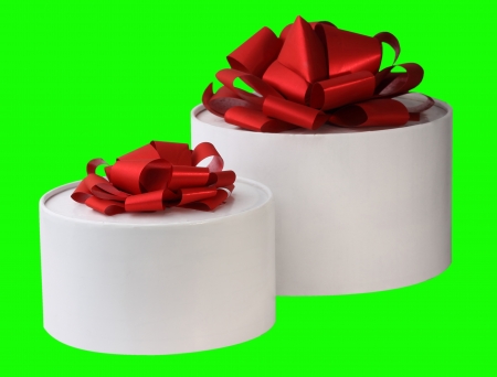 The image of two white gift round boxes with red tapes is on a green の写真素材
