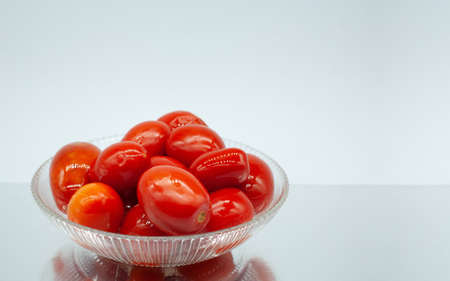 Whole pickled tomatoes in a transparent glass dish. Tomatoes are on a mirror surface, close-up on a light background. Marinated tomatoes.の写真素材