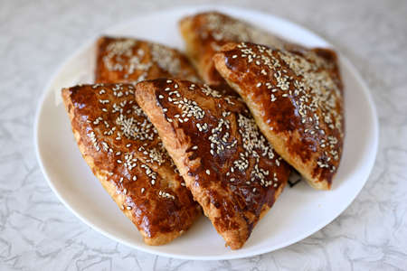 Step by step instructions. Step ten. How to make a puff pastry product with meat at home. Ready-made homemade puff pastry sprinkled with sesame seeds with meat filling on a plate.の写真素材