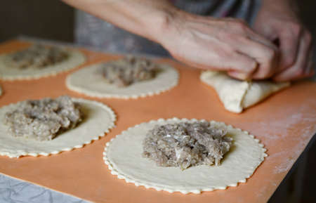 Step by step instructions. Step six. How to make a puff pastry product with meat at home. Join the edges of the dough into a triangular shape. Woman's hands close up. Soft focus.の写真素材