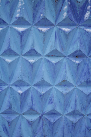 Blue concrete wall. Volumetric pattern in the form of triangles. Snow on the wall. Close-up.