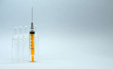 Medical background. Ampoules with solution for injection and a syringe without a cap stand on the table, ready to use.の写真素材
