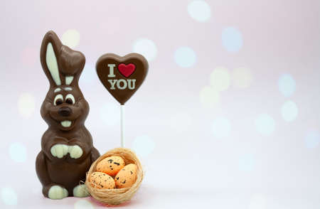 Symbol of Easter. Chocolate rabbit and decorative eggs in a nest. Chocolate heart on a stick with the inscription "I love you". Festive background with bokeh.の写真素材