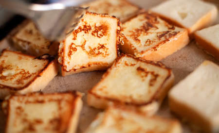 Yummy square-shaped croutons fried in a pan. Homemade food, breakfast. White bread in egg fried in a pan with butter. Home kitchen. Croutons flip with a fork.の写真素材