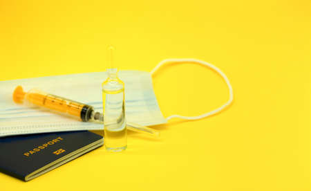 The concept of vaccination and travel. International passport, mask, syringe and ampoule with a medicinal substance (vaccine) .Yellow background.Traveling during COVID-19 pandemic.の写真素材