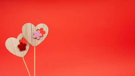 Two wooden decorative hearts on sticks. Red background. Space for text on the right. Love and valentine's day concept. Festive postcard.の写真素材