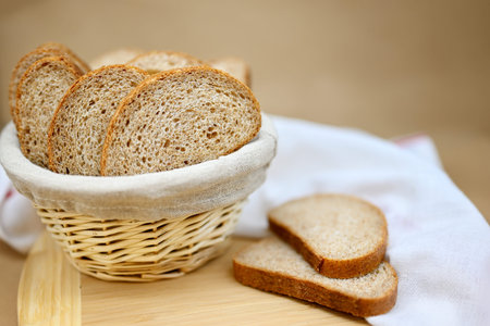Fresh cereal bread in a wicker basket. The bread is sliced. Beige background, wooden board, linen...