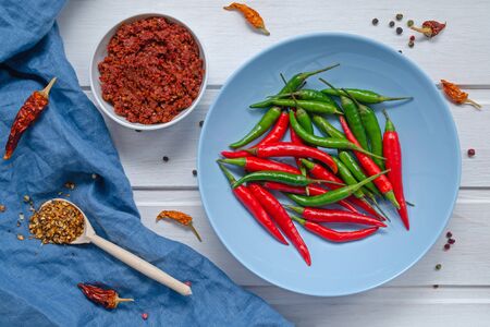 Hot chilli pepper sauce paste harissa, traditional Tunisia, Moroccan, Arabic cuisine adjika ,chili pepper spices and fresh red and green chilli peppers in blue plate, over white background. close-upの写真素材