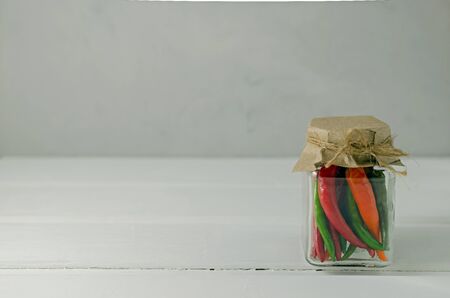 Marinated chili peppers red green yellow in a jar. Stocks of food. Top view. On a light background. Copy space.の写真素材