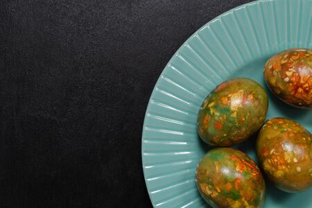 modern trendy marble Easter eggs of original coloring on a blue plate on a black slate background closeup with a copy spaceの写真素材
