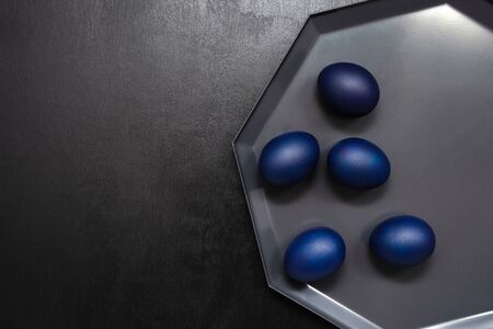 Classic trendy Easter eggs in classic blue on a dark tray on a black background with place for text. minimalism. dark key.の写真素材