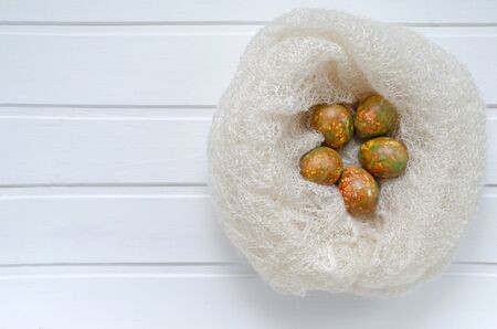 fashionable modern Easter multicolored, originally painted, marbled eggs in a warm woolen nest on a white wooden background with copy spaceの写真素材