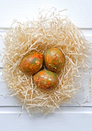 fashionable modern Easter multi-colored, originally painted, marble eggs in a nest on a white wooden background with copy space shot from aboveの写真素材