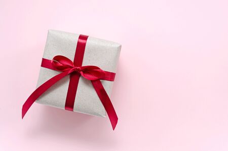 gift wrapped in paper from environmentally friendly paper from recycled waste with a red satin ribbon with a bow on a delicate pink background with copy space. zero waste concept. universal greetingsの写真素材