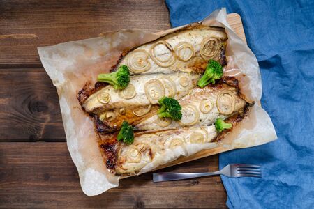 Oven baked mackerel with chopped onion rings and broccoli on a dark wooden background with a blue napkin. keto diet and healthy eating. copy spaceの写真素材
