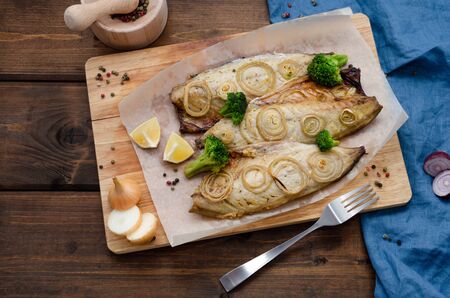 tender mackerel baked in the oven with chopped onion rings, broccoli and lemon on a dark wooden background with a blue napkin and fork. keto diet and healthy eating. copy spaceの写真素材