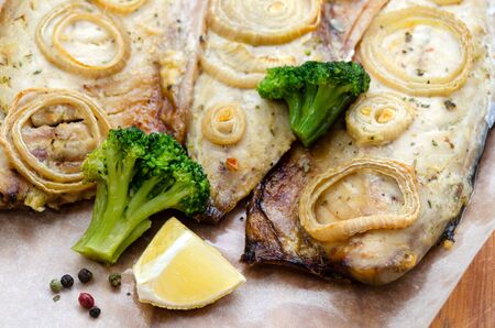 closeup fresh tender baked mackerel with rings of chopped onion, broccoli and lemon on a dark wooden cutting board in baking paper. keto and flexitarian diet and healthy eating. copy spaceの写真素材