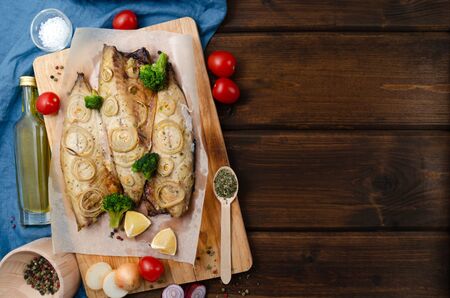 Oven baked mackerel with chopped onion rings, broccoli, tomatoes and lemon on a dark wooden background with a blue napkin. keto and flexitarian diet and healthy eating. copy spaceの写真素材