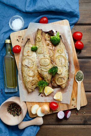 Oven baked mackerel with chopped onion rings, broccoli, tomatoes and lemon on a dark wooden background with a blue napkin. keto and flexitarian diet and healthy eating. copy spaceの写真素材