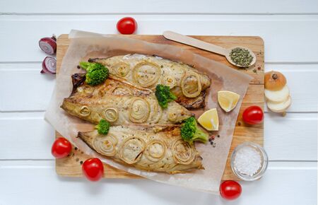tasty buttery fish mackerel saba with lemon, sliced on filet with tomatoes, onions and broccoli in a bouillagi for baking on a cutting board on a white wooden background, close-upの写真素材
