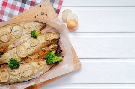 fresh tender baked mackerel with rings of chopped onion, broccoli and lemon on a dark wooden cutting board in baking paper. keto and flexitarian diet and healthy eating. with place for textの写真素材