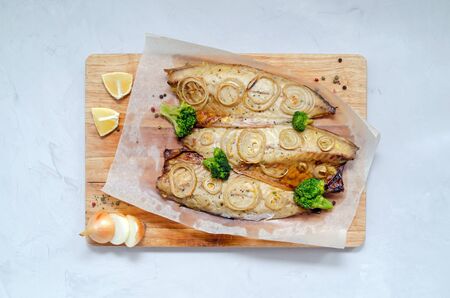 fresh tender baked mackerel with rings of chopped onion, broccoli and lemon on a light background in baking paper. keto and flexitarian diet and healthy eating. with place for textの写真素材