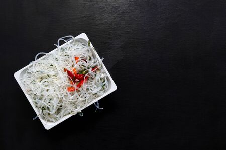 Asian glass rice noodles with vegetables and herbs on a white deep square plate on a black slate background with copy space. oriental cuisine, veganism, lean food, flexitarianism, peganism, keto dietの写真素材
