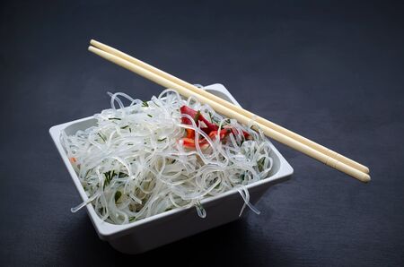 Asian glass rice noodles with vegetables and herbs on white deep square plate on black slate background with place for text. oriental cuisine, veganism, lean food, flexitarianism, peganism, keto dietの写真素材
