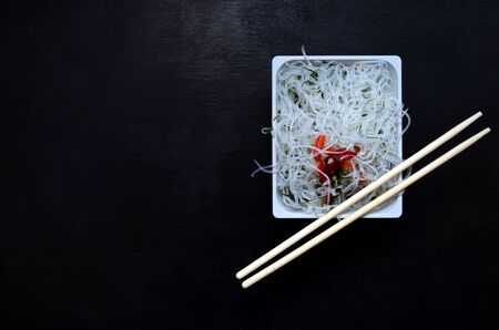 Glass funchose noodles and bamboo sticks on a white square plate on a black slate background with copy space. oriental asian cuisine, veganism, lean food, flexitarianism, peganism, keto dietの写真素材