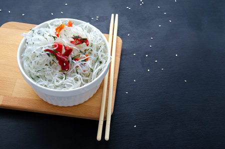 Asian glass fungoza rice noodles and bamboo sticks on a wooden board in a white round bowl with...