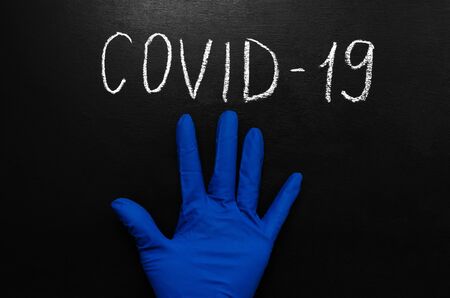 Coronavirus concept. The inscription in white chalk on a black slate background and a blue medical sterile glove. Epidemic of coronavirus infection. Pandemic. with place for text or image placementの写真素材