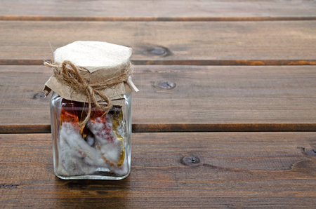ugly spoiled rotten red and green chilli hot peppers in the mold in a glass jar on a wooden...