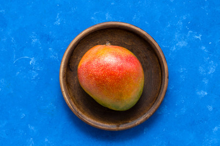 Ripe juicy fruit of the Brazilian mango from the tropics on a plate on a blue background with copy...