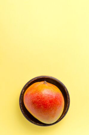 Fresh juicy mango on a brown clay plate on a yellow uniform background. exotic fruits healthy eating and lifestyle minimalism fruit diet slimming close-up with place for textの写真素材