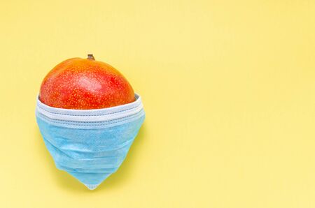 coronavirus concept covid 19 fruit is protected from the virus with a medical mask on a yellow background with copy space. a medical mask is put on a mango close upの写真素材