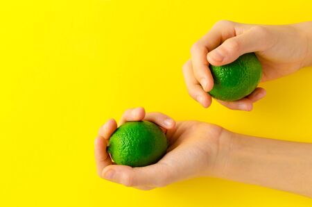 A children's hand holding limes in her hands on yellow background. This fresh fruit contains vitamin c and can be used as an ingredients for many dishes. Healthy background concept. close upの写真素材