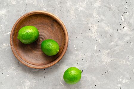 Fresh juicy limes on a brown clay plate on a grey background. citrus vitamin C healthy diet and lifestyle minimalism close up copy spaceの写真素材