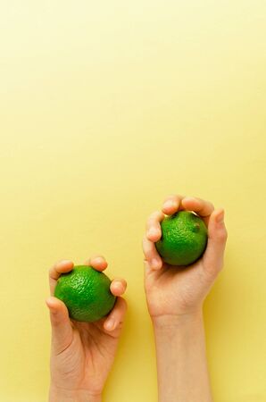 children's hand holding limes in her hands on yellow background. This fresh fruit contains vitamin c and can be used as an ingredients for many dishes. Healthy background concept. close upの写真素材