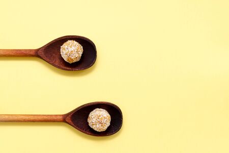 Healthy organic energy balls with nuts and honey in coconut flakes. vegan vegetarian raw snack or food sports snack in wooden spoons on a yellow background.の写真素材
