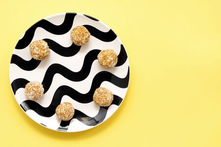 round sweets. Energy balls in coconut flakes on a black and white plate on a yellow background. healthy food sports snack. view from above . copy spaceの写真素材
