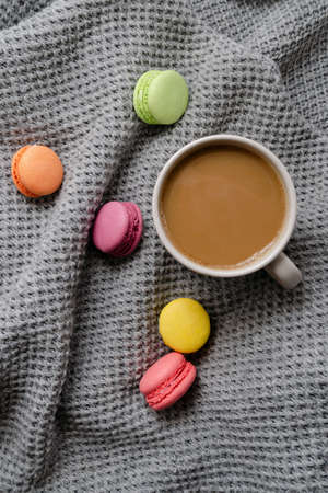 Background with gray plaid, coffee, cappuccino and multicolored appetizing macaroons, top view, flat lay. home comfort, warmth, care, tenderness.の写真素材